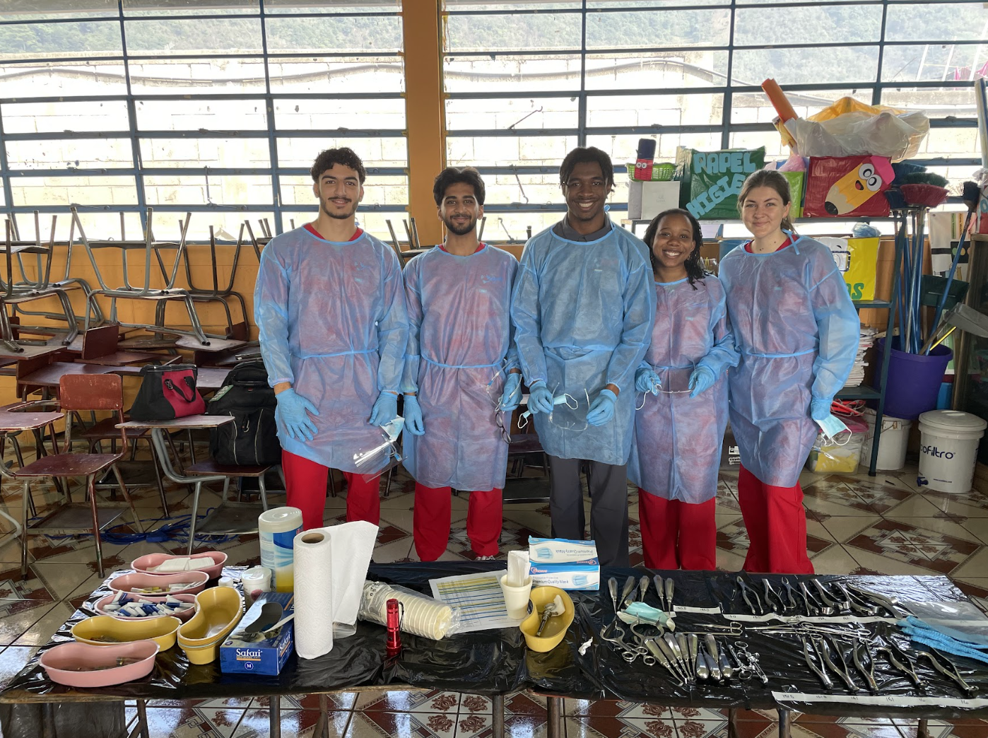 Five students in medical scrubs in front of a table of health equipment